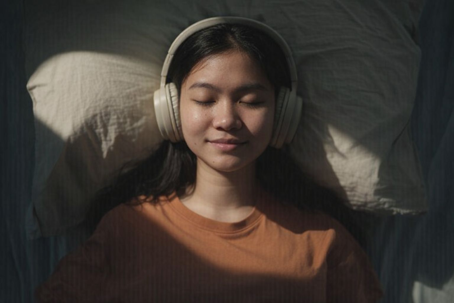 Nainen kuuntelee äänikirjaa kuulokkeilla leväten tyynyllä.