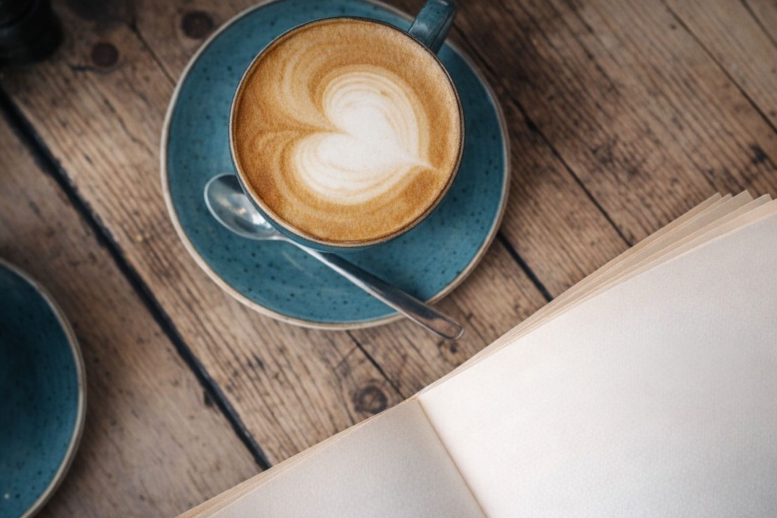 Sydänkuvioinen latte ja avoin kirja puisella pöydällä.